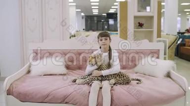 漂亮的少女坐在儿童粉红色的床上，拥抱<strong>家具</strong>店的毛绒玩具。 年<strong>轻</strong>女孩选择<strong>家具</strong>